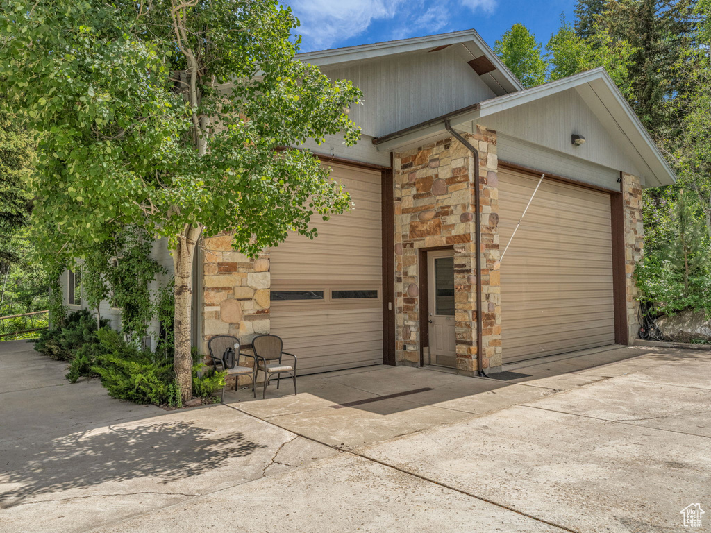 View of side of property with concrete driveway, stone siding, and an attached garage