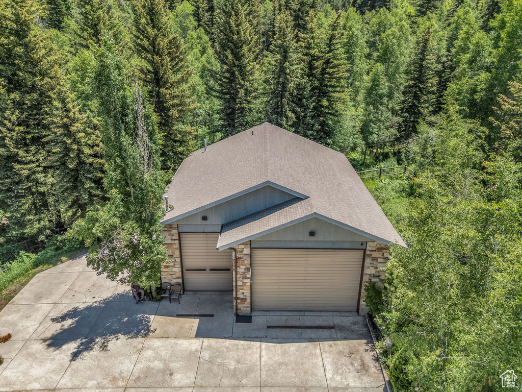 View of front of home with roof with shingles, stone siding, a forest view, concrete driveway, and an attached garage