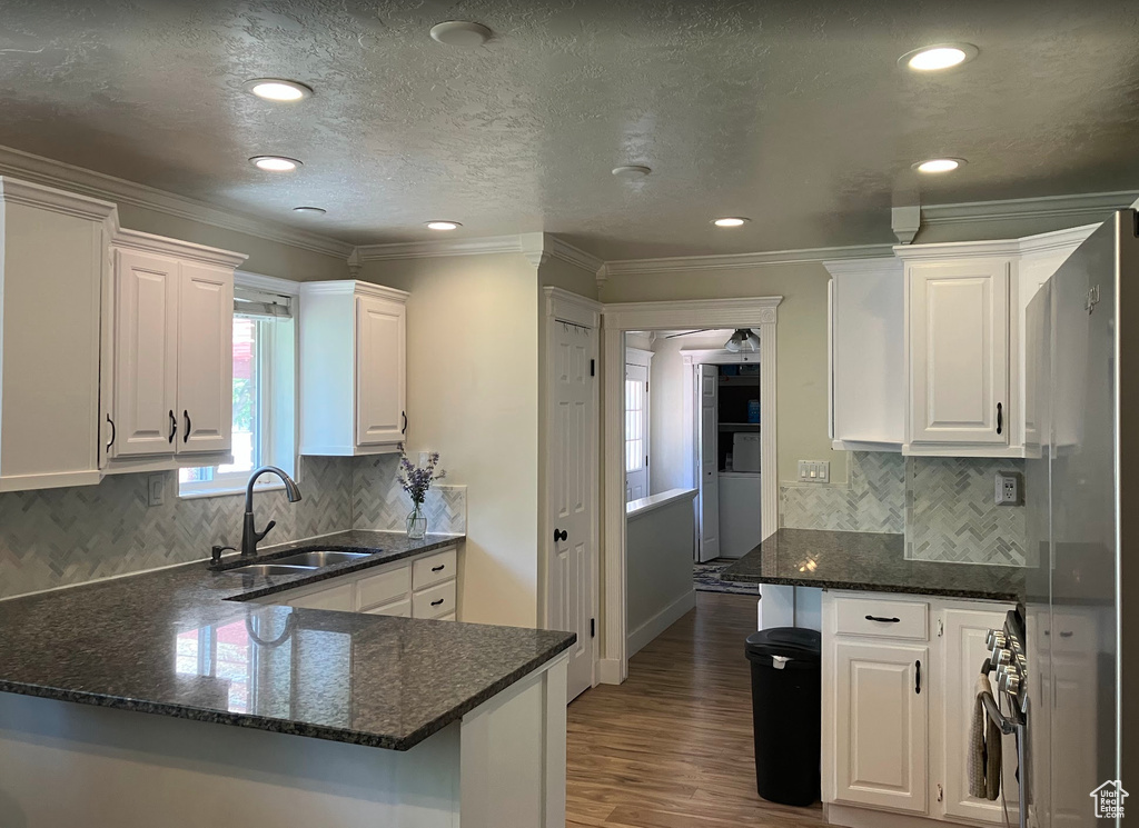 Kitchen with white cabinetry, wood finished floors, dark stone counters, recessed lighting, and ornamental molding