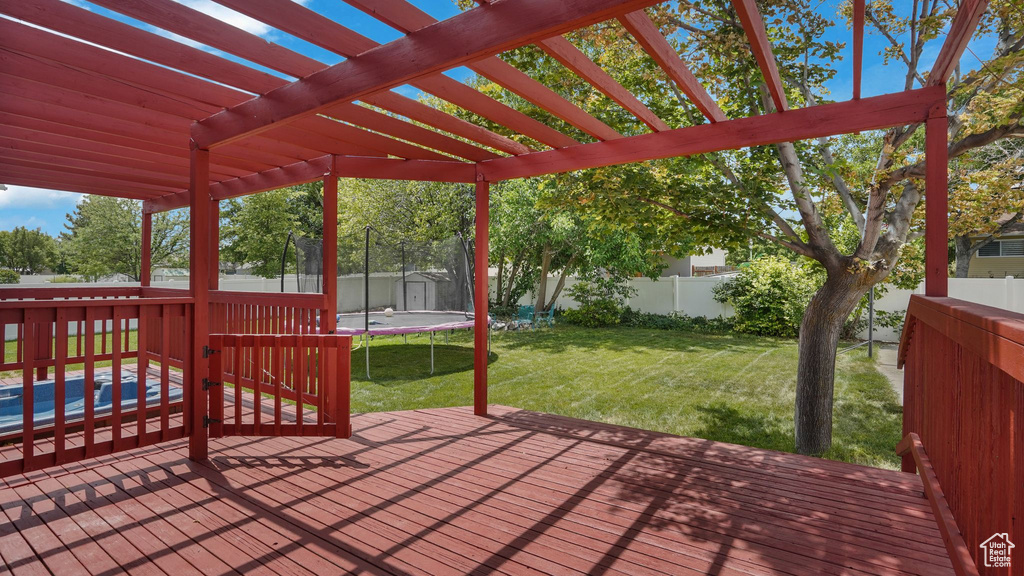 Wooden terrace with a trampoline, a fenced backyard, and a pergola