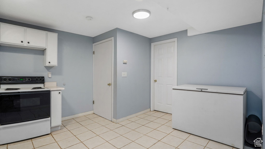 Kitchen with electric range oven, white fridge, light countertops, white cabinetry, and light tile patterned floors