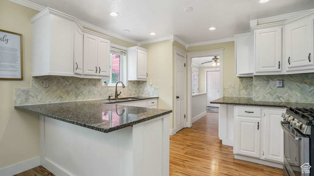 Kitchen with gas stove, white cabinets, light wood finished floors, dark stone countertops, and recessed lighting