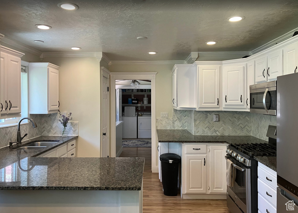 Kitchen with appliances with stainless steel finishes, independent washer and dryer, white cabinetry, ornamental molding, and wood finished floors