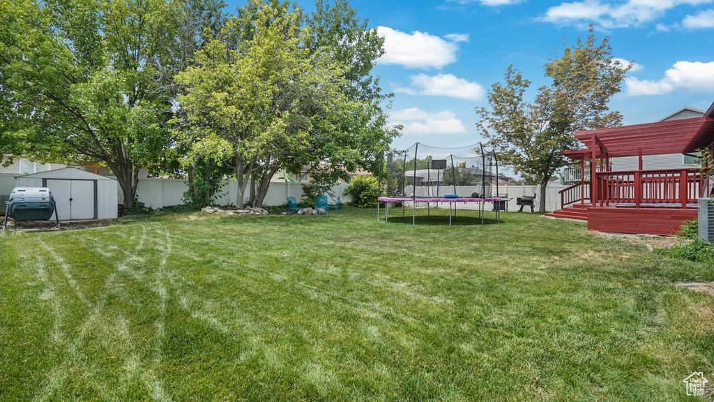Fenced backyard featuring a storage unit, a trampoline, and a wooden deck