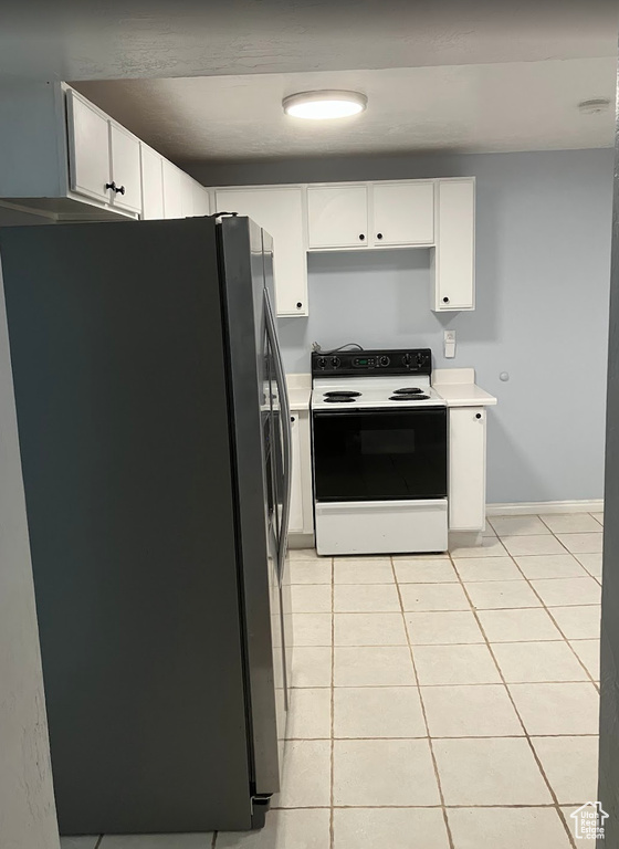 Kitchen featuring stainless steel fridge, electric range oven, light countertops, light tile patterned floors, and white cabinets