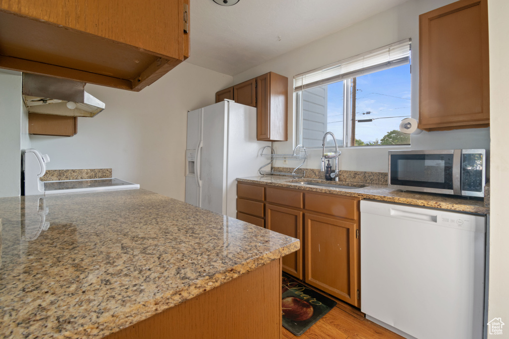 Kitchen featuring white appliances, under cabinet range hood, light wood-type flooring, and brown cabinetry
