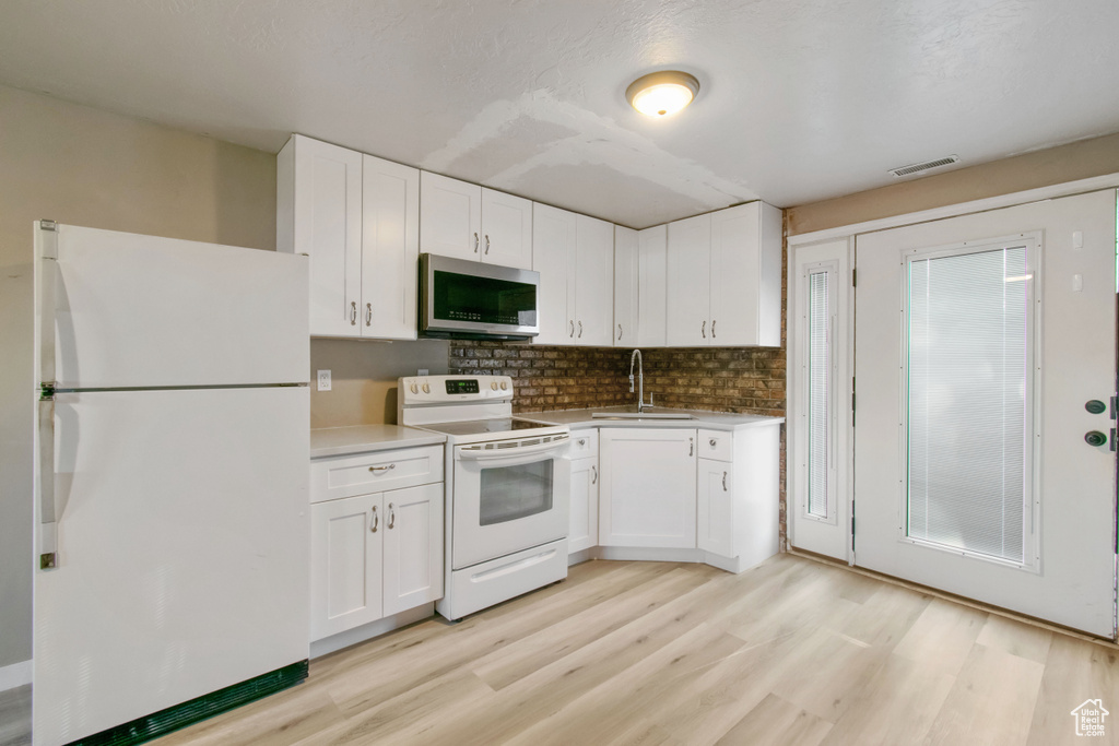 Kitchen with white appliances, light wood-style floors, tasteful backsplash, and white cabinetry