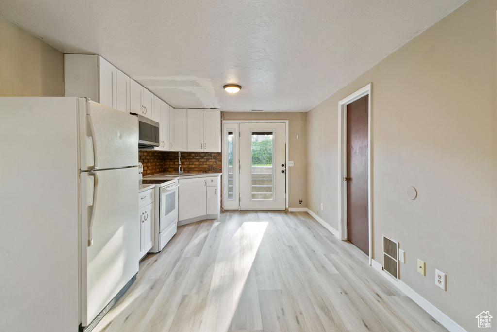Kitchen with white appliances, white cabinets, tasteful backsplash, and light wood-style floors