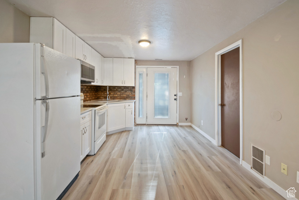 Kitchen with white appliances, white cabinetry, light wood-style floors, decorative backsplash, and light countertops