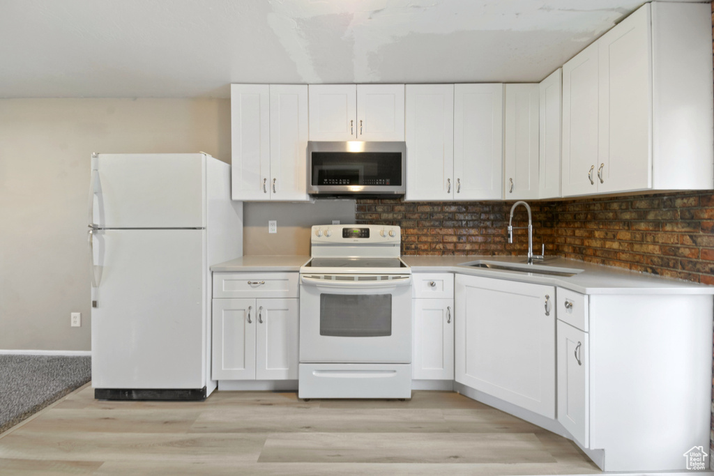 Kitchen with white appliances, light wood-style flooring, white cabinets, tasteful backsplash, and light countertops