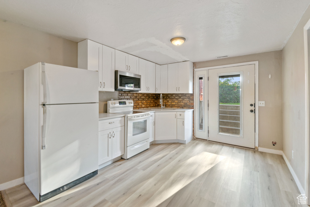 Kitchen with white appliances, light wood-type flooring, white cabinetry, and decorative backsplash