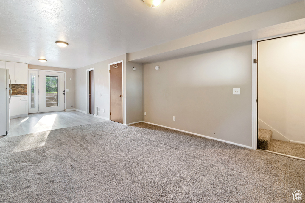 Unfurnished living room featuring light colored carpet and stairway
