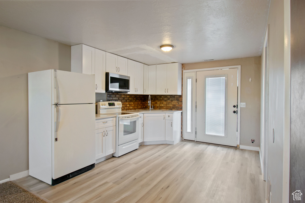 Kitchen featuring white appliances, white cabinetry, backsplash, and light wood-type flooring