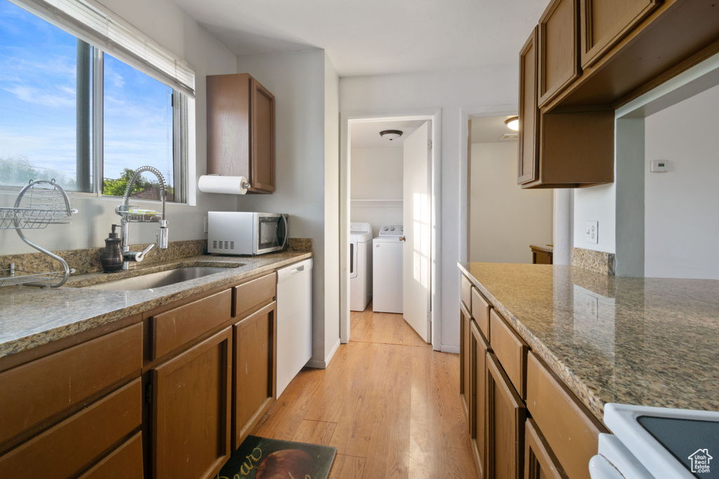 Kitchen with stainless steel microwave, washer and clothes dryer, dishwasher, light wood-style floors, and stone countertops