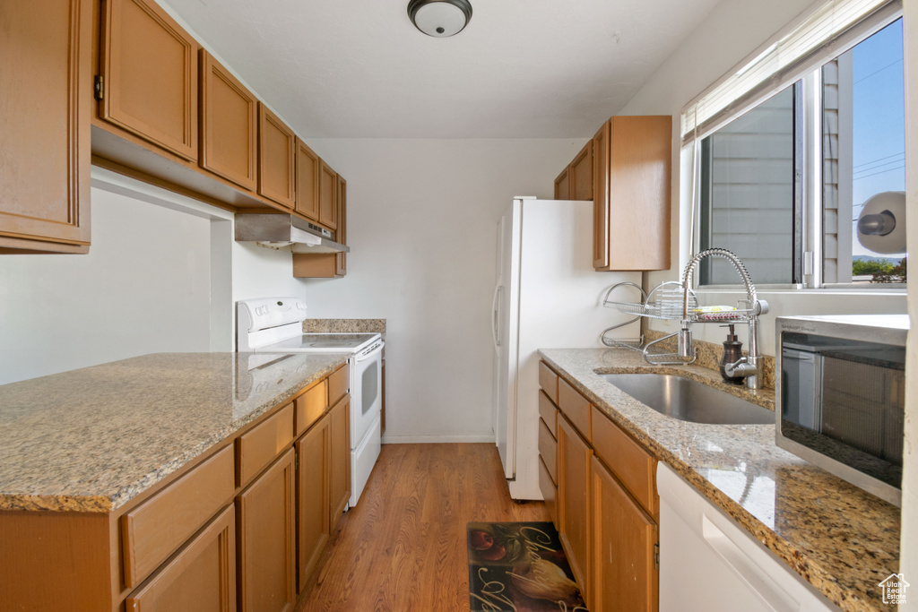 Kitchen featuring white appliances, light wood-type flooring, under cabinet range hood, light stone countertops, and brown cabinets