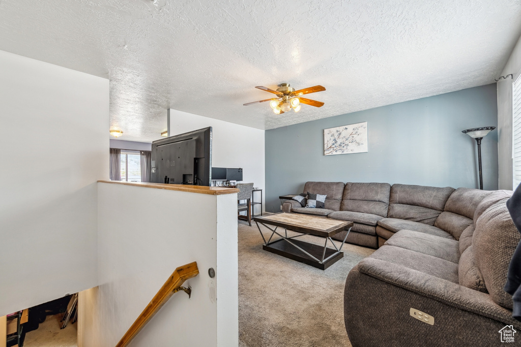 Carpeted living room featuring a ceiling fan and a textured ceiling