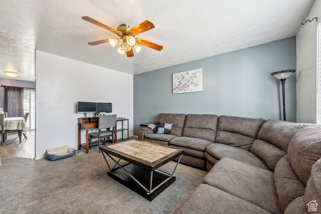 Carpeted living room featuring a textured ceiling, ceiling fan, and an office area