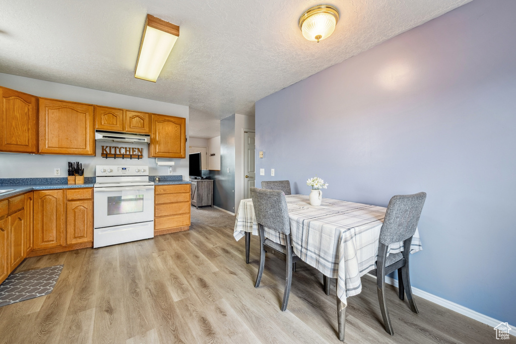 Kitchen featuring white electric range oven, under cabinet range hood, light wood-style flooring, brown cabinets, and a textured ceiling