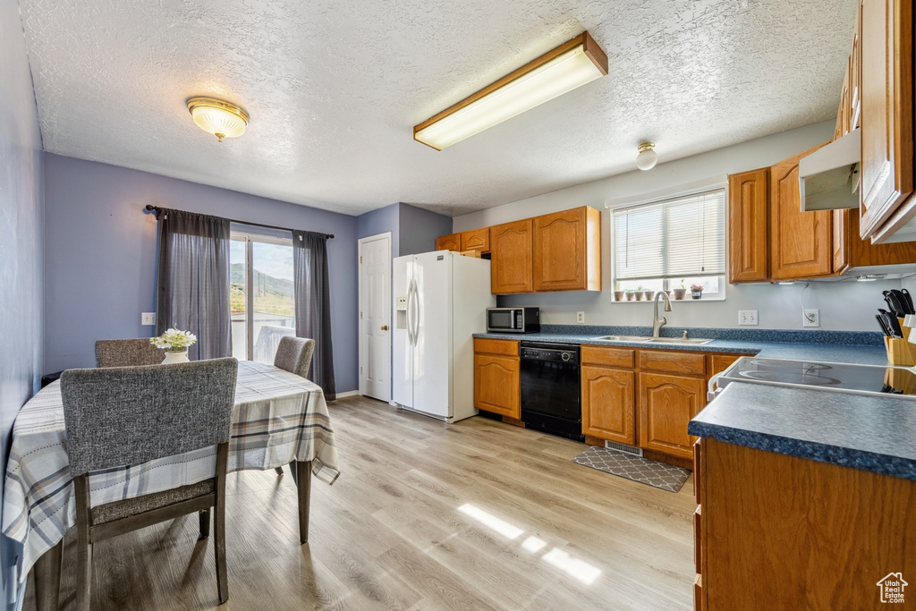 Kitchen featuring black dishwasher, white fridge with ice dispenser, stainless steel microwave, exhaust hood, and dark countertops