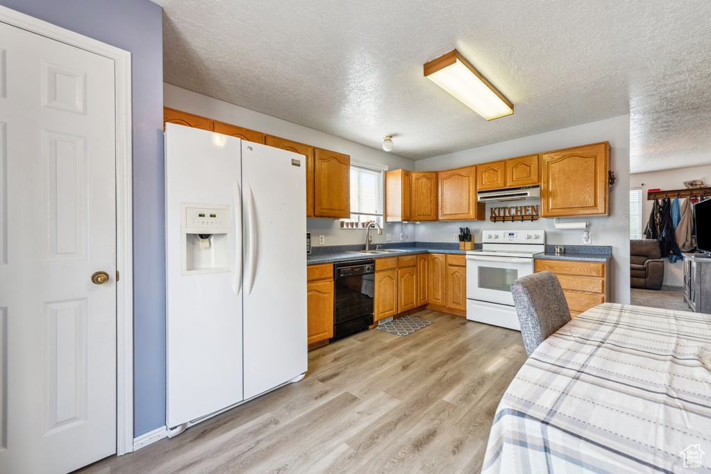 Kitchen with white appliances, under cabinet range hood, a textured ceiling, light wood-type flooring, and dark countertops