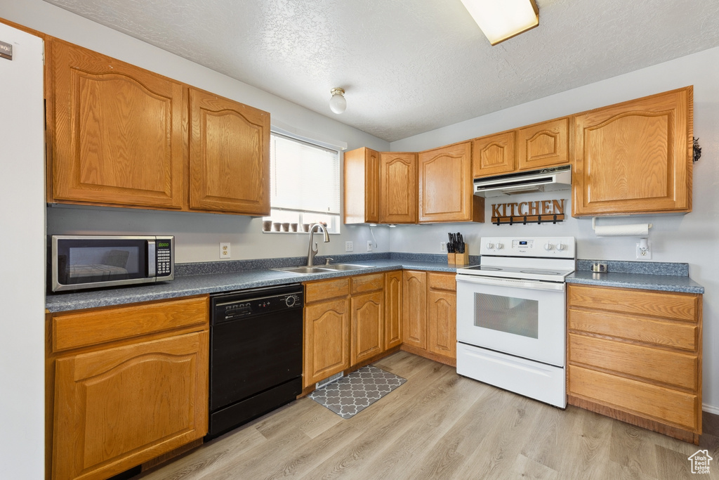 Kitchen featuring white appliances, under cabinet range hood, light wood finished floors, dark countertops, and a textured ceiling