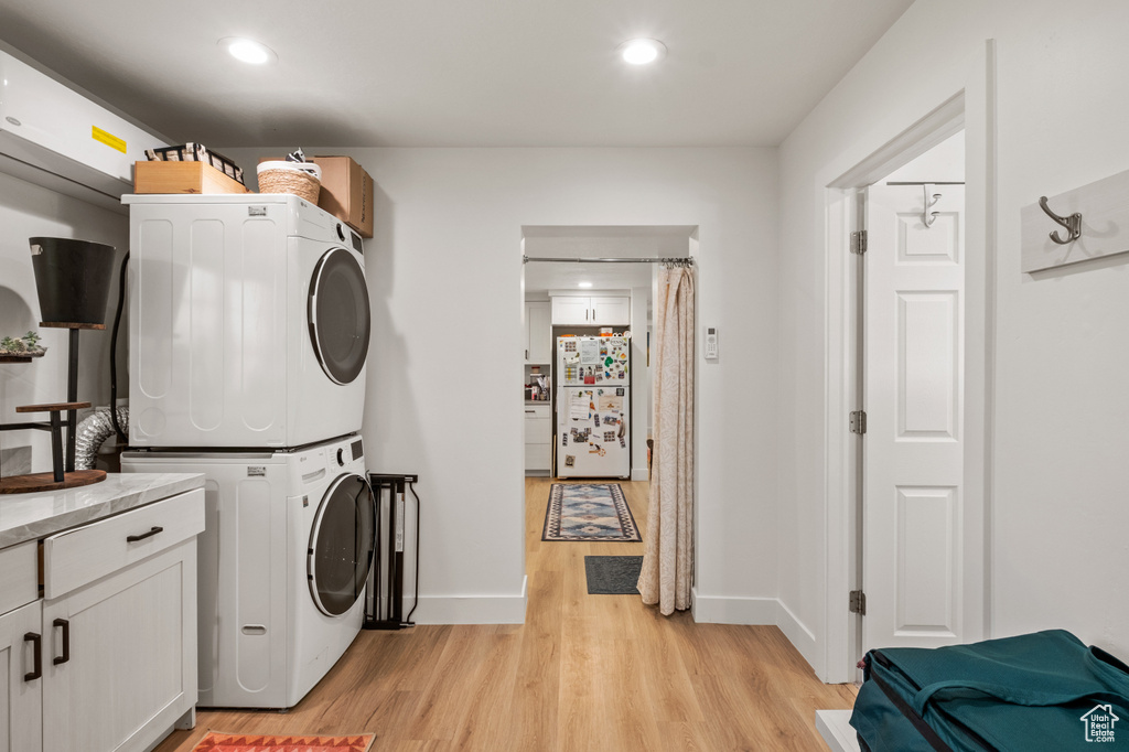 Laundry room with stacked washer / drying machine, light wood finished floors, recessed lighting, and cabinet space