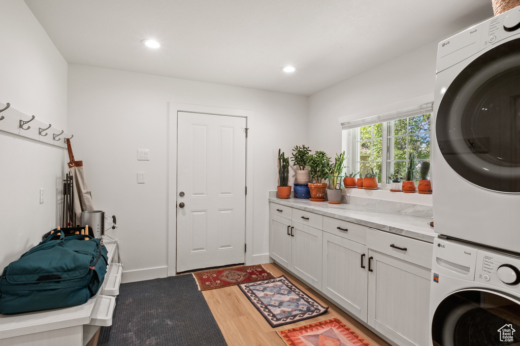 Laundry area with stacked washer / dryer, cabinet space, light wood-type flooring, and recessed lighting