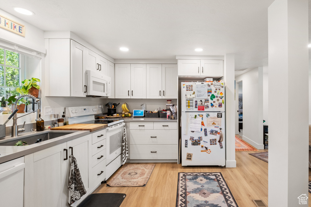 Kitchen featuring white appliances, light wood finished floors, white cabinets, and recessed lighting