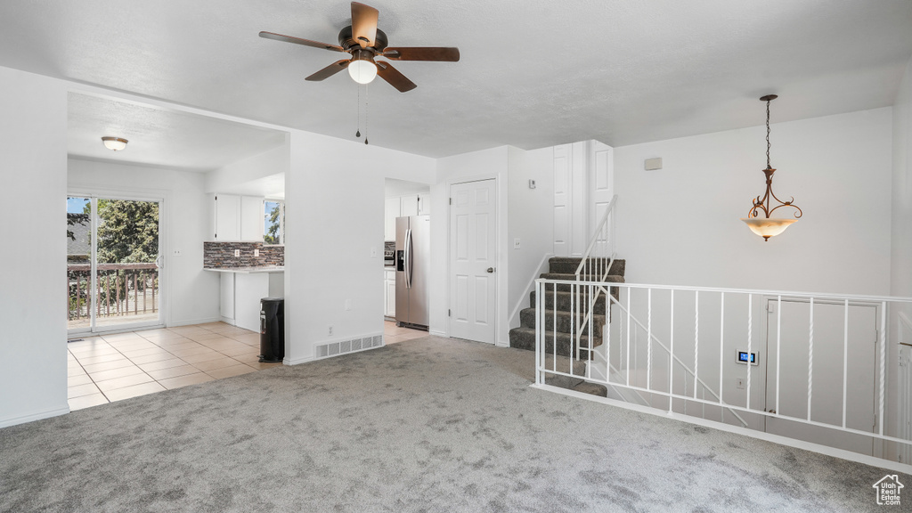 Empty room with ceiling fan, light carpet, and light tile patterned flooring