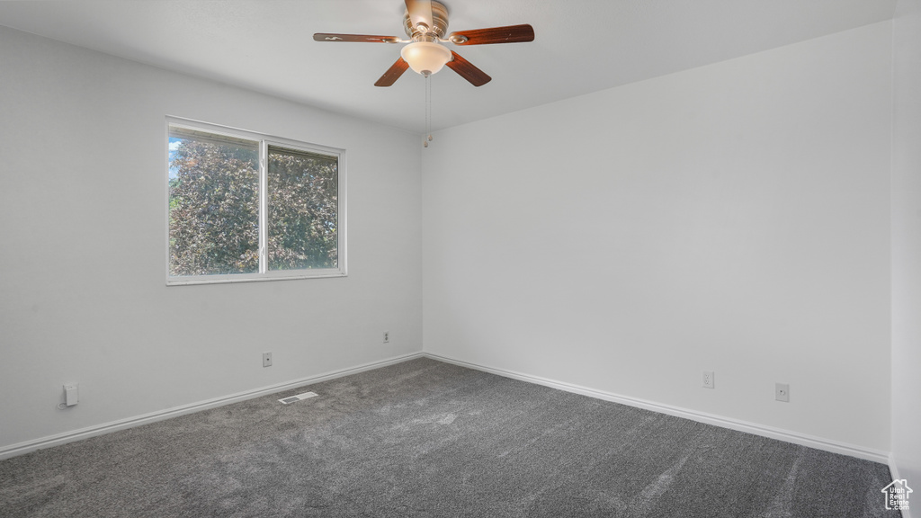 Spare room with a ceiling fan and dark colored carpet