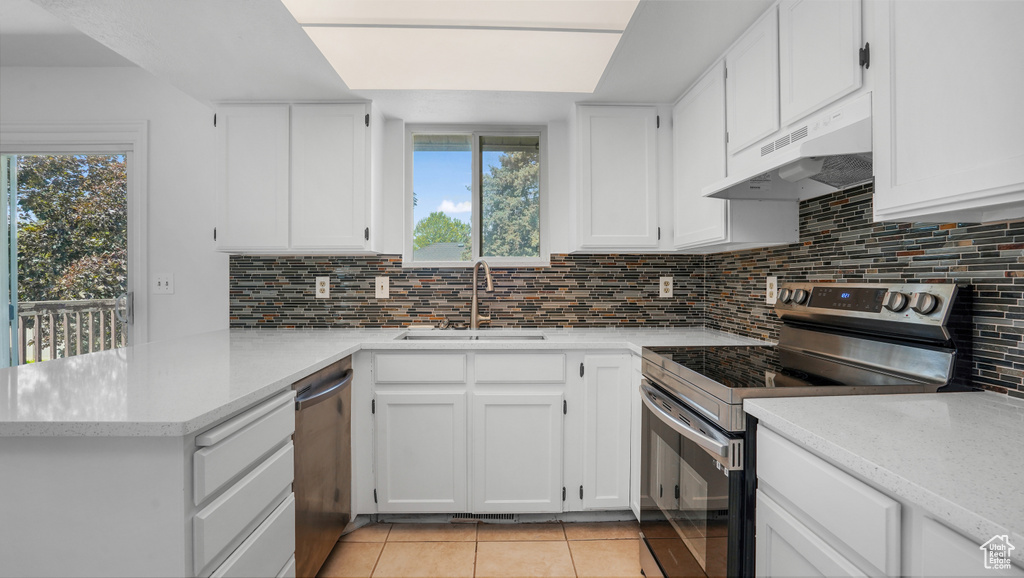 Kitchen featuring stainless steel appliances, under cabinet range hood, a peninsula, light tile patterned floors, and white cabinets