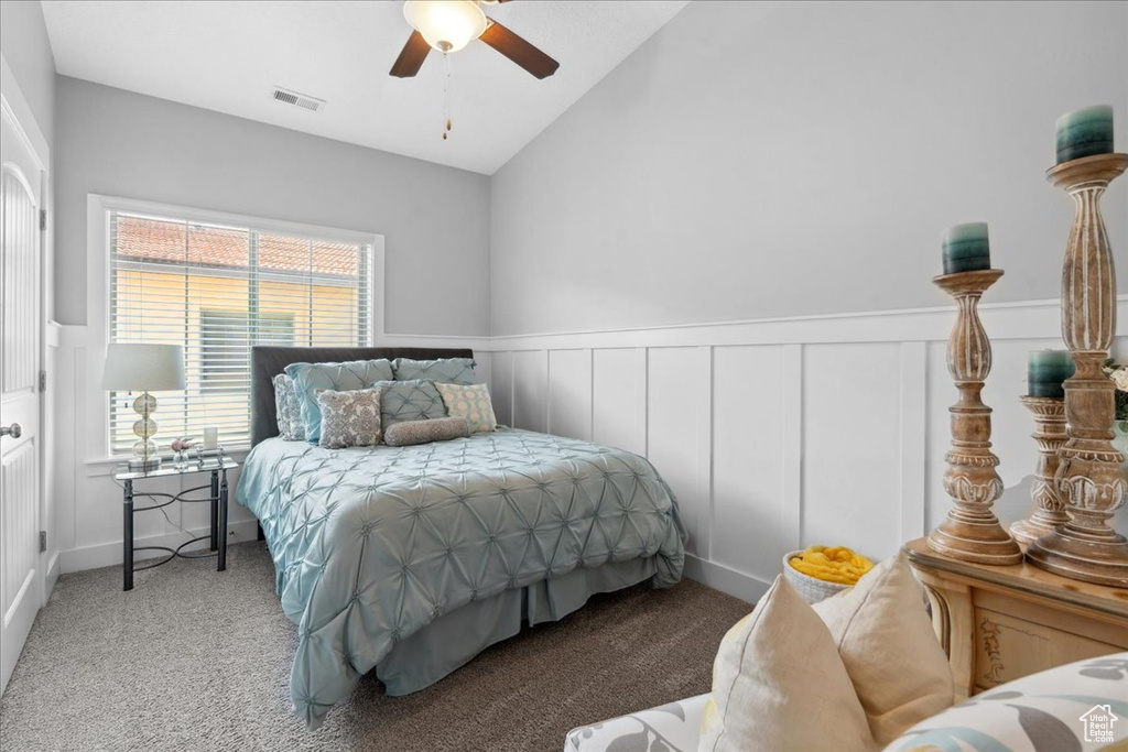 Carpeted bedroom with a decorative wall, vaulted ceiling, a wainscoted wall, and ceiling fan