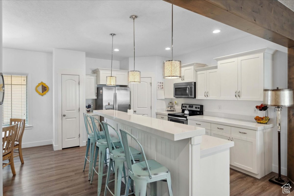 Kitchen featuring stainless steel appliances, white cabinets, a kitchen island, a breakfast bar area, and light countertops