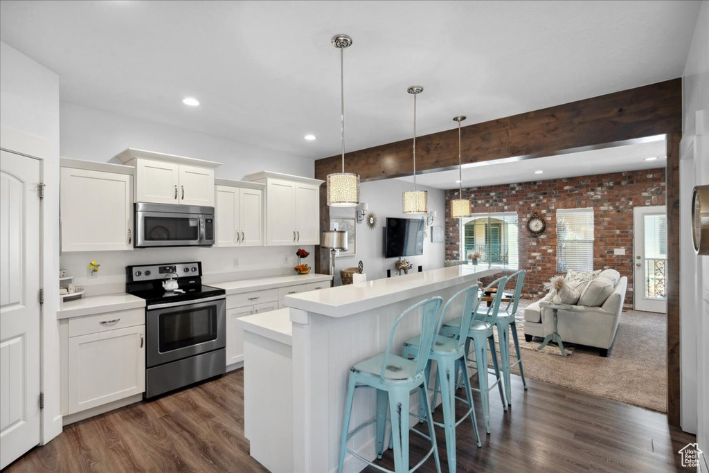 Kitchen with appliances with stainless steel finishes, brick wall, a kitchen island, light countertops, and dark wood-style flooring