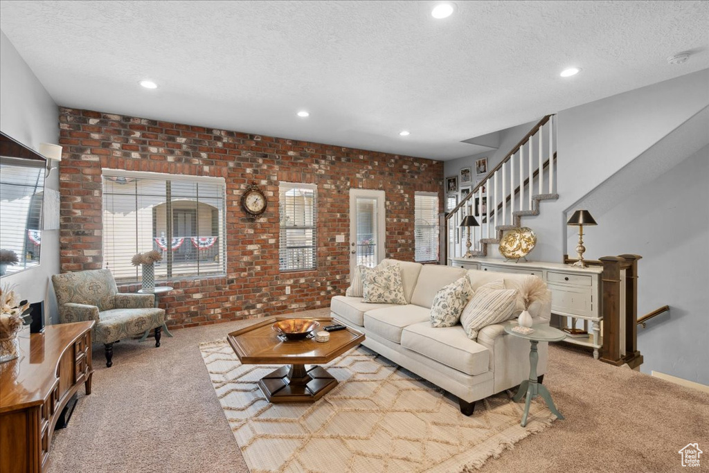 Living room with carpet floors, a textured ceiling, recessed lighting, brick wall, and stairs