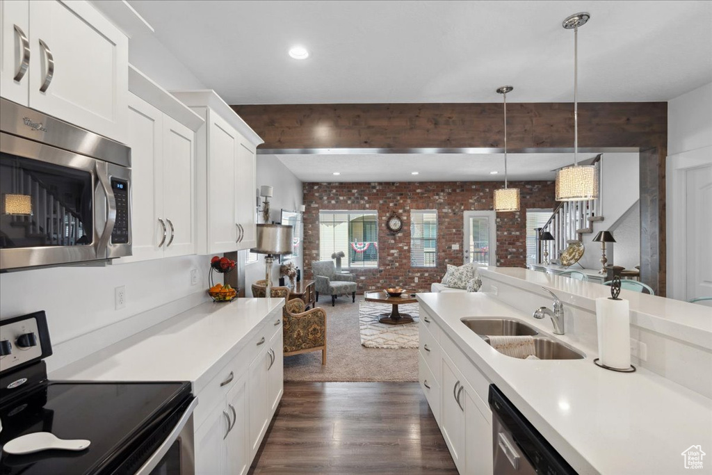 Kitchen featuring appliances with stainless steel finishes, brick wall, open floor plan, dark wood-style flooring, and light countertops