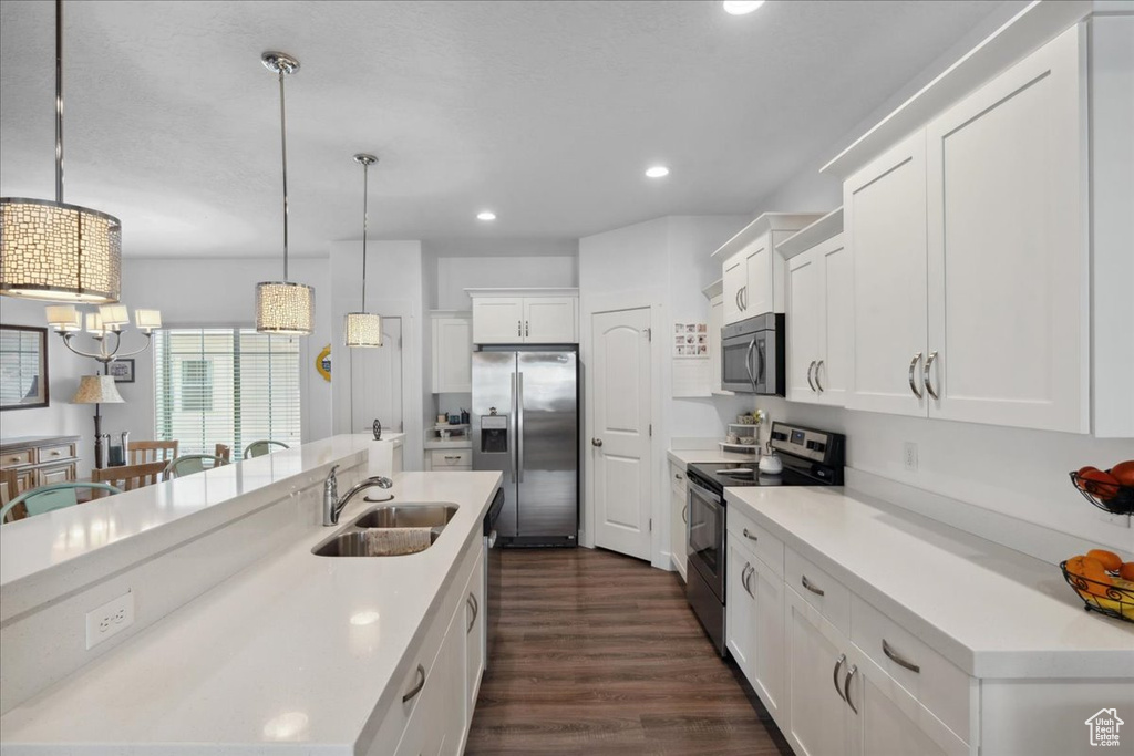 Kitchen featuring appliances with stainless steel finishes, dark wood-style floors, white cabinetry, a kitchen island with sink, and hanging light fixtures