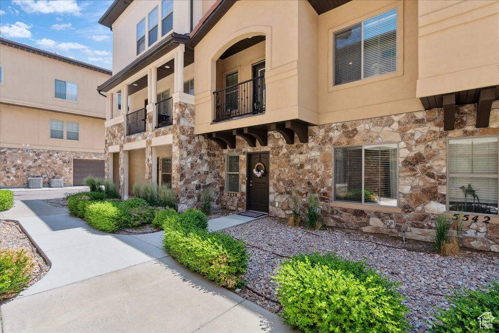 View of front of home with stone siding, a balcony, and stucco siding