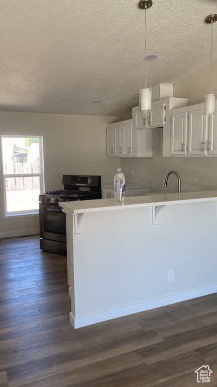 Kitchen featuring stainless steel range with gas cooktop, a breakfast bar area, a textured ceiling, dark wood-type flooring, and white cabinets