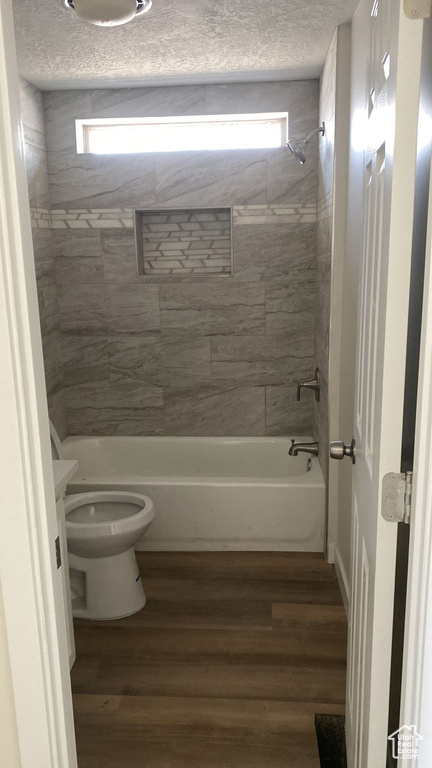 Bathroom featuring plenty of natural light, wood finished floors,  shower combination, and a textured ceiling