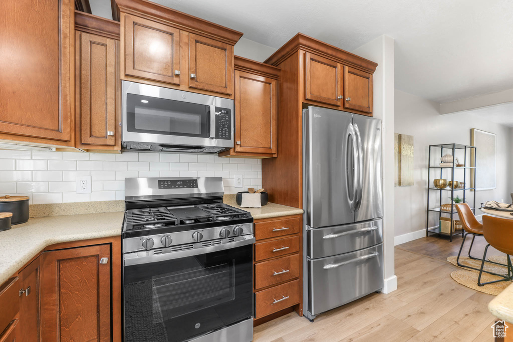Kitchen with appliances with stainless steel finishes, light wood-style flooring, light countertops, and decorative backsplash