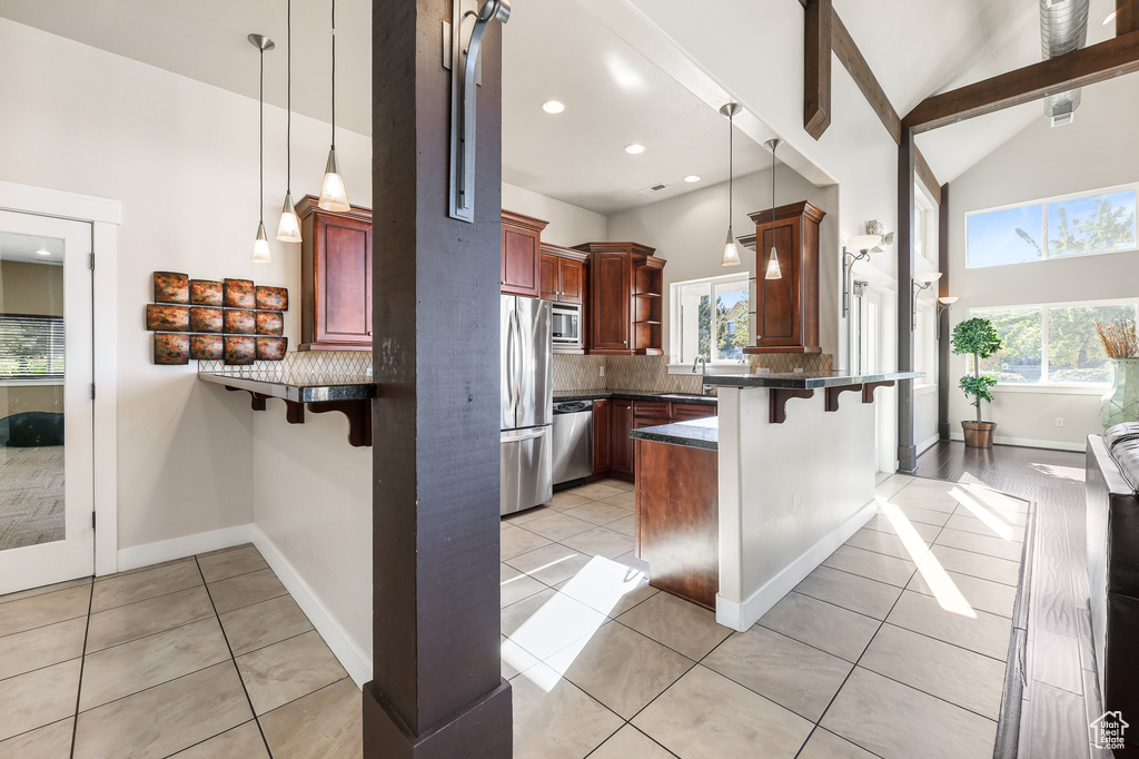 Kitchen with dark countertops, a peninsula, appliances with stainless steel finishes, plenty of natural light, and high vaulted ceiling