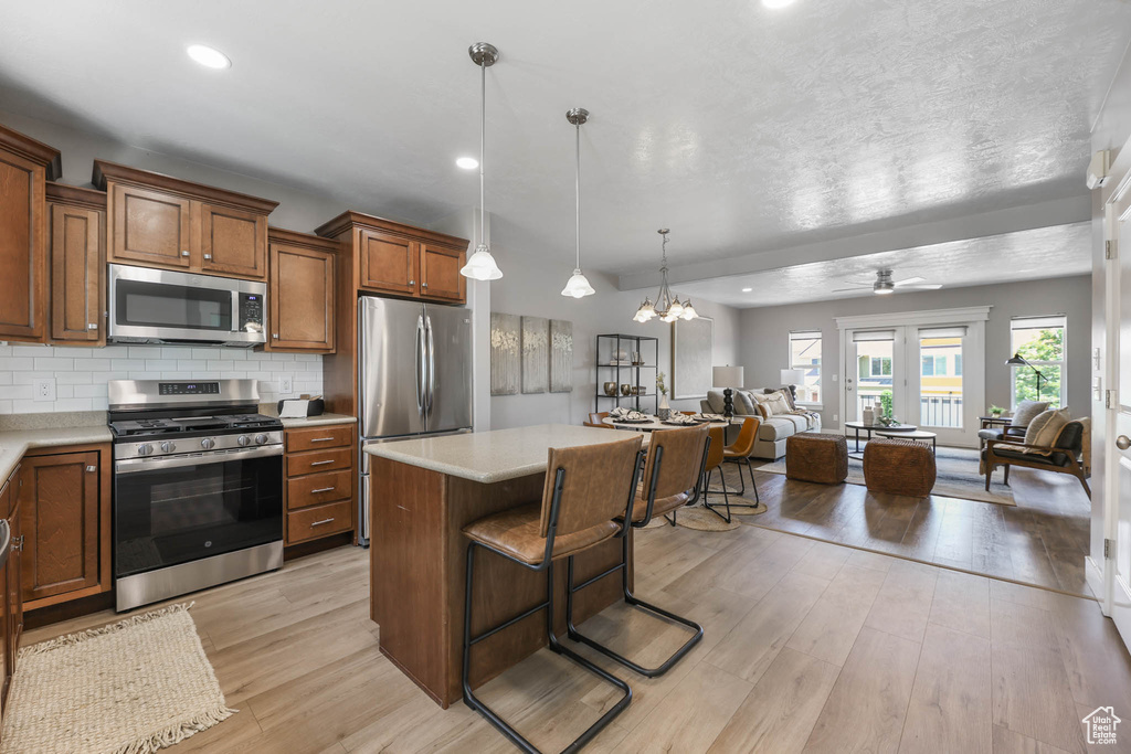 Kitchen with stainless steel appliances, open floor plan, light wood finished floors, light countertops, and brown cabinets