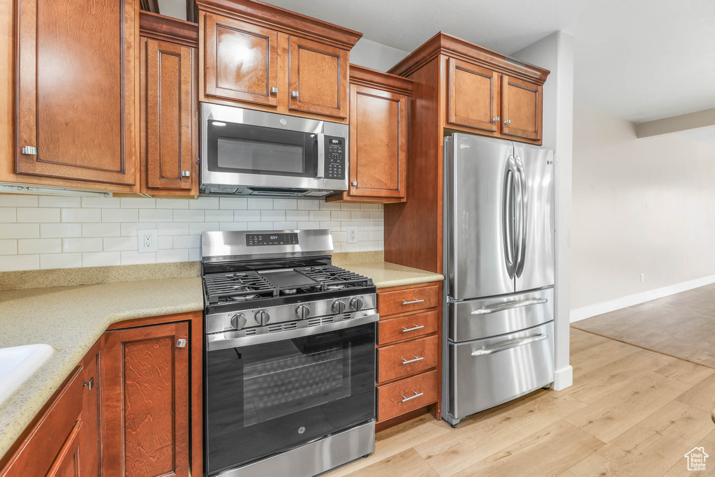Kitchen featuring appliances with stainless steel finishes, light wood finished floors, tasteful backsplash, and brown cabinets