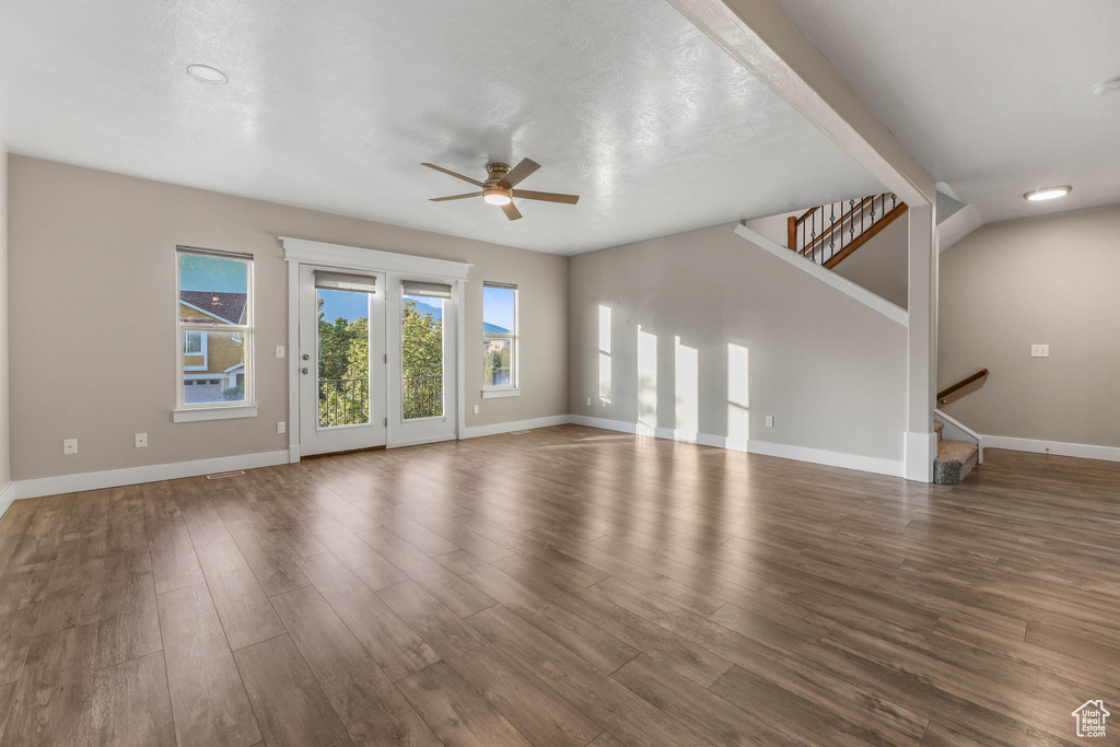 Unfurnished living room featuring ceiling fan, plenty of natural light, stairway, and wood finished floors