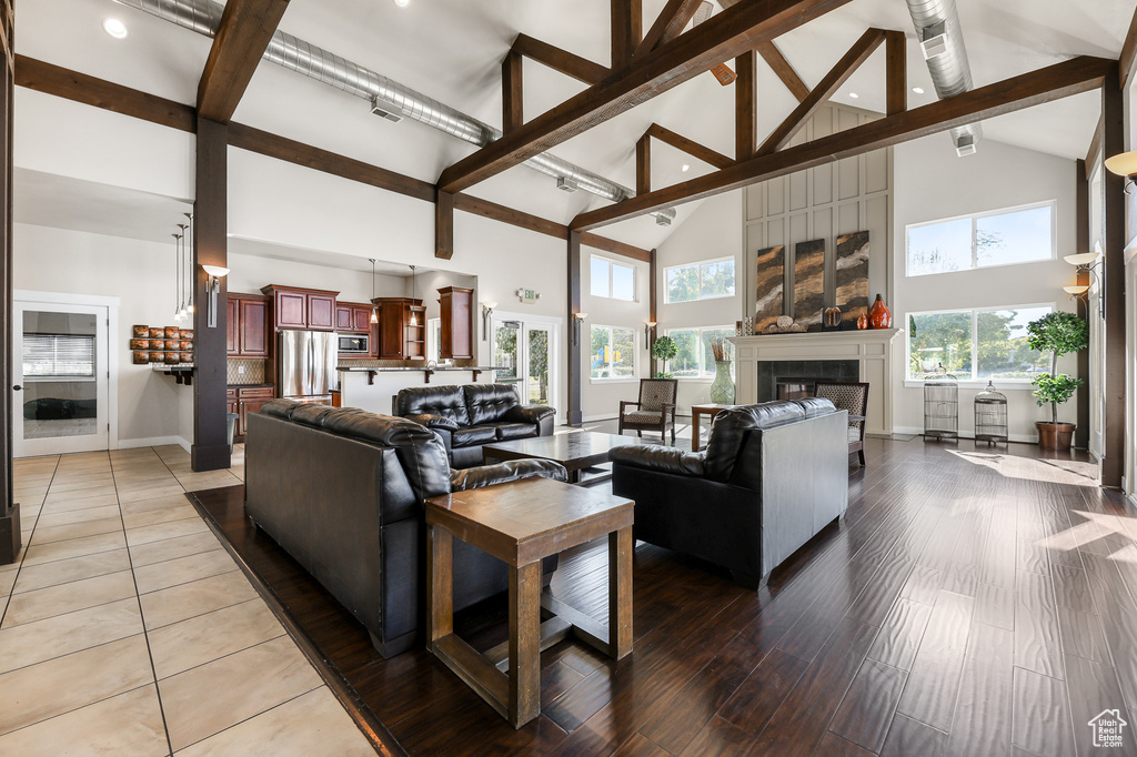 Living area with high vaulted ceiling, a glass covered fireplace, beam ceiling, light tile patterned floors, and recessed lighting