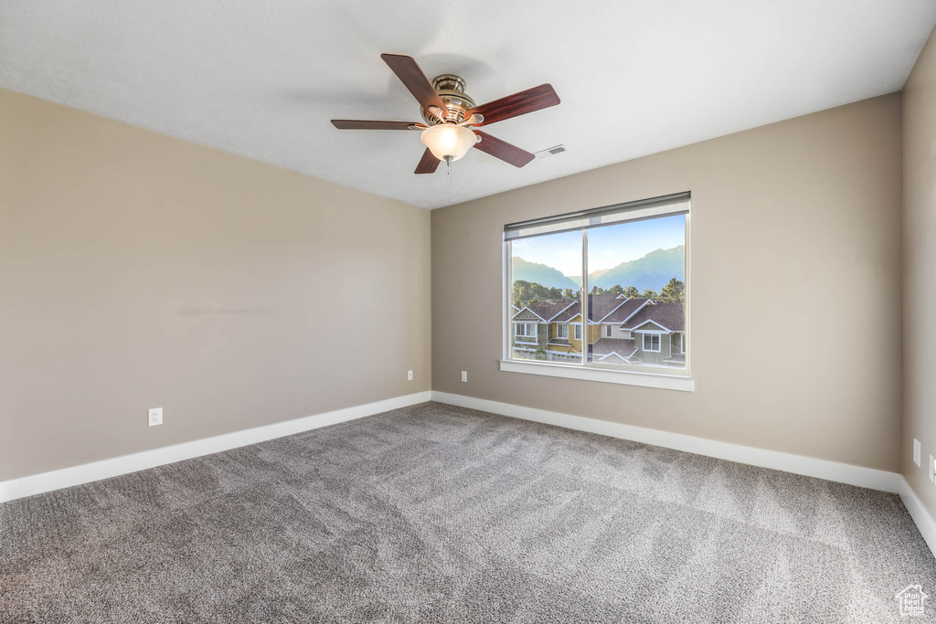 Carpeted empty room featuring a ceiling fan and baseboards