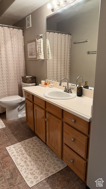 Full bath with vanity, a textured ceiling, and stone finish flooring