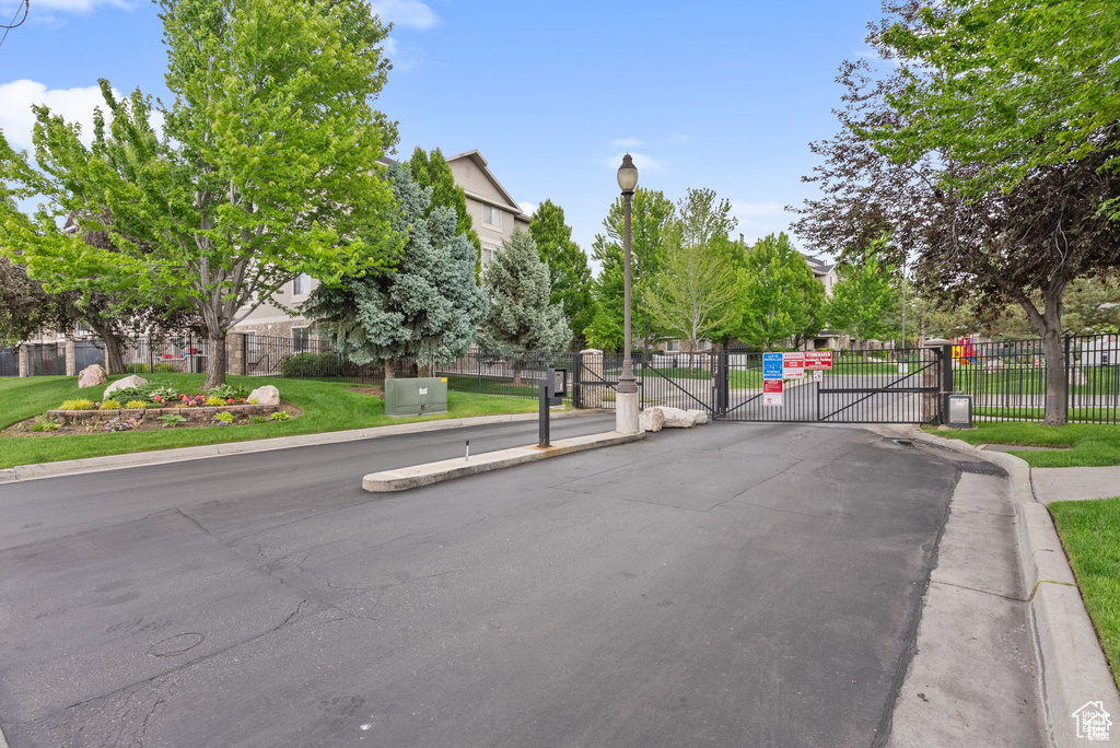 View of asphalt road featuring a gate, street lighting, a gated entry, and curbs