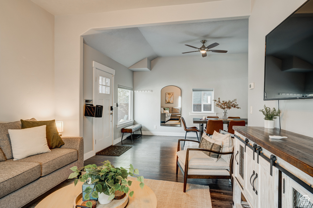 Living area featuring a ceiling fan, dark wood-type flooring, arched walkways, and lofted ceiling